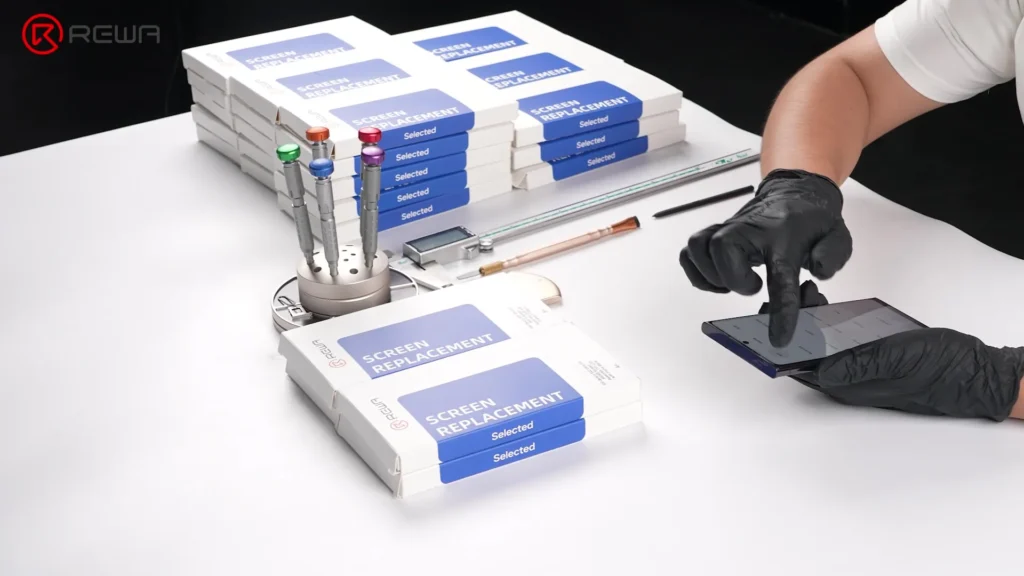 the evolution of samsung aftermarket screens: from incell lcd to advanced 1:1 oled Technician testing a smartphone screen next to stacks of REWA screen replacement boxes and repair tools